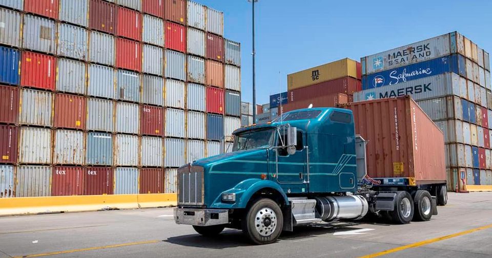 Camión de carga frente a contenedores logístico-portuarios.